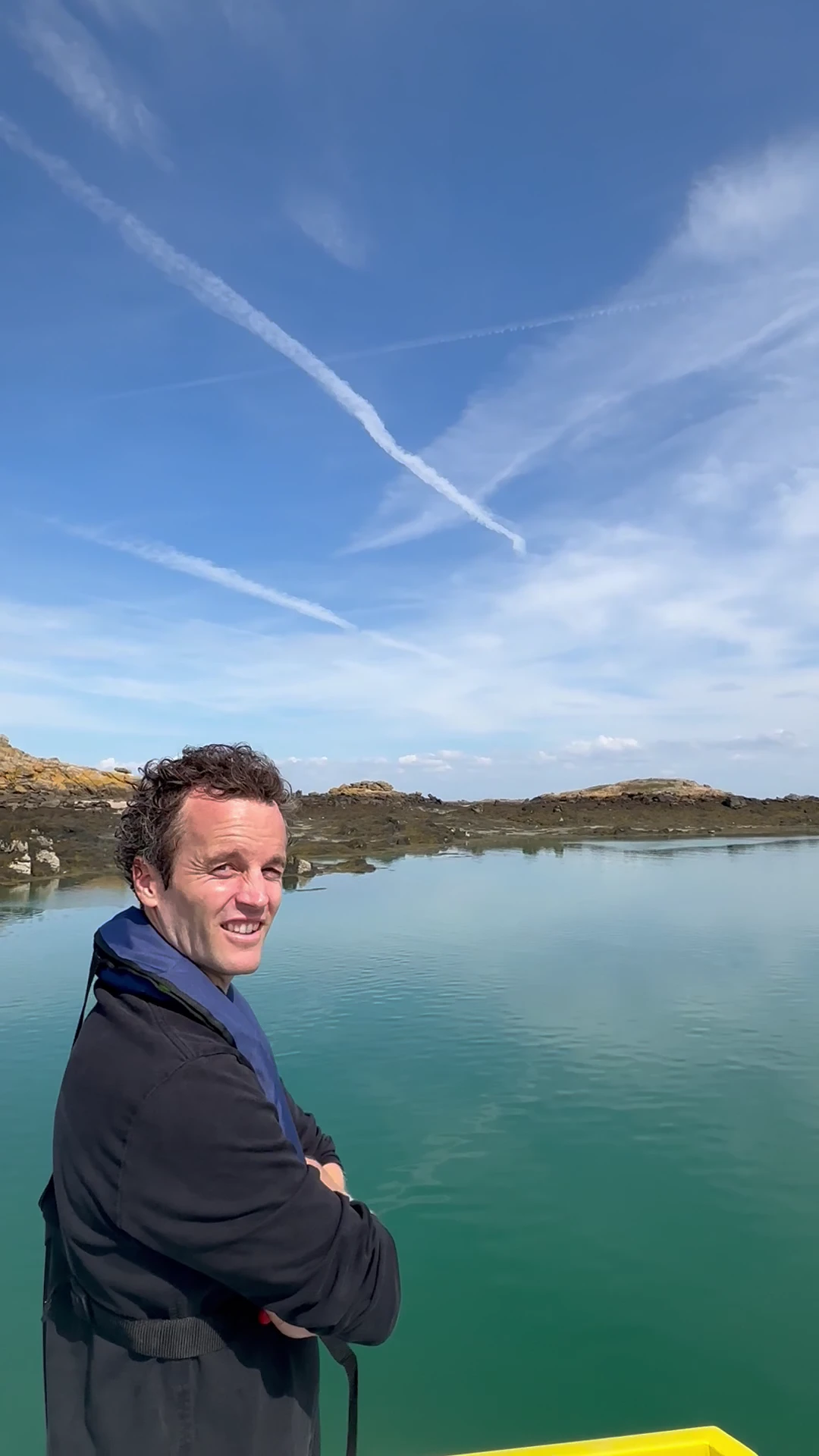 Adrien smiling aboard a boat with calm Atlantic tidal water and rocky islands behind him